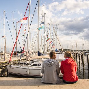 Schleswiger Stadthafen in Abendstimmung mit Perosnen siteznden an der Kaimauer.